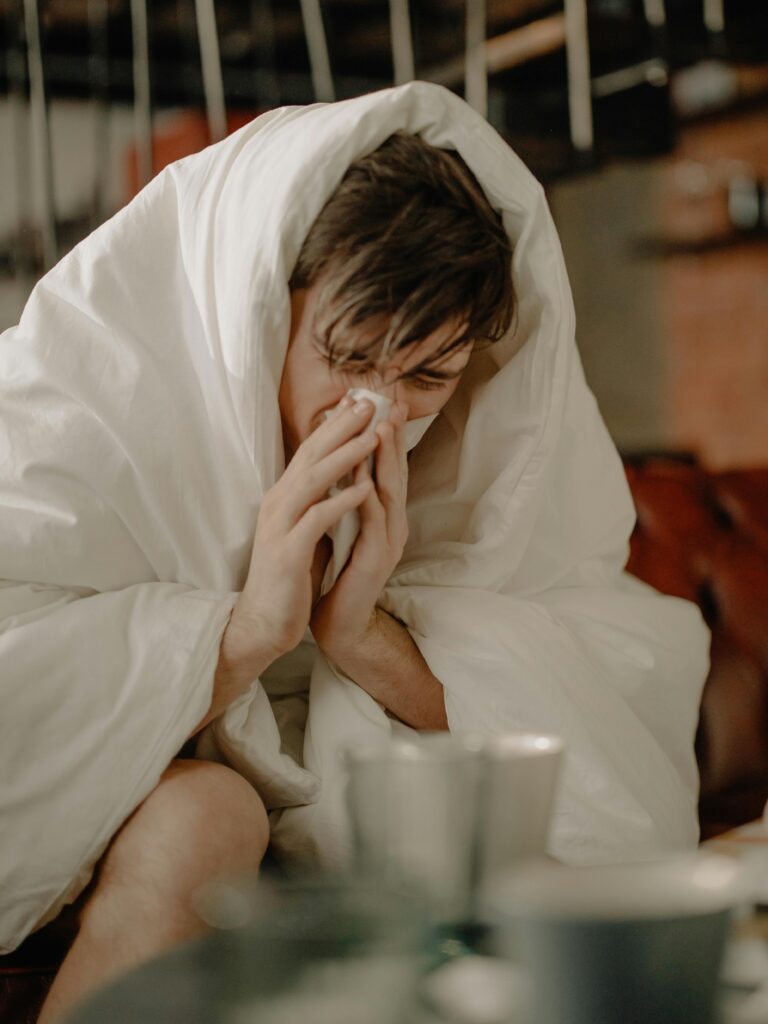 A young man wrapped in a blanket sneezes, indicating illness or cold symptoms.