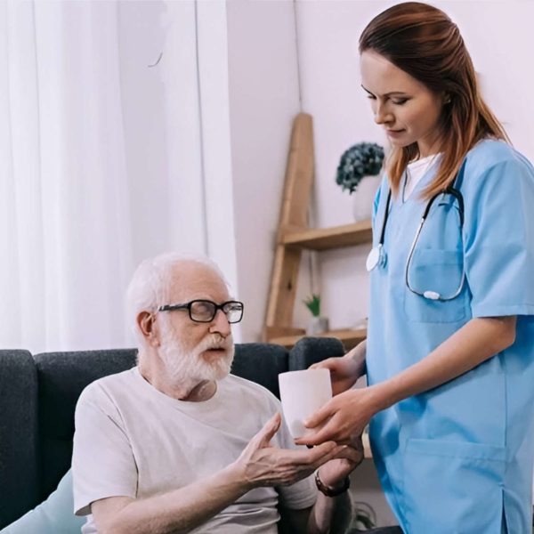 Nurse assisting elderly man with medication at home.